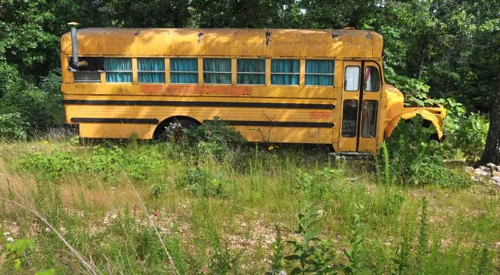 Старый желтый школьный автобус с занавесками и трубой в поле