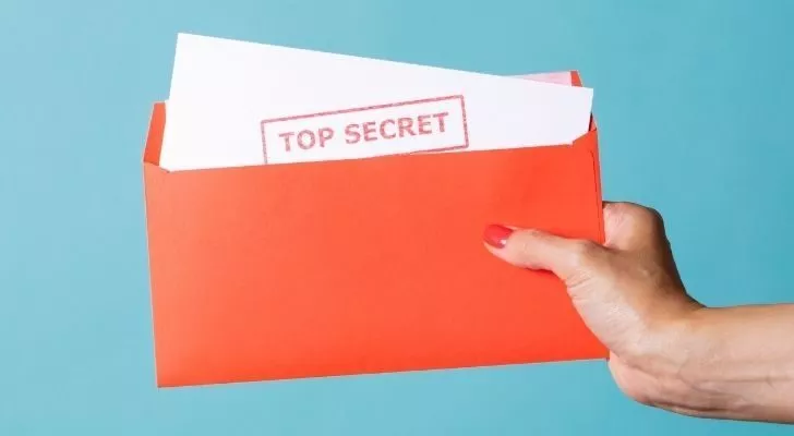 Человек держит в руках лист бумаги со словами'top secret' written on it.