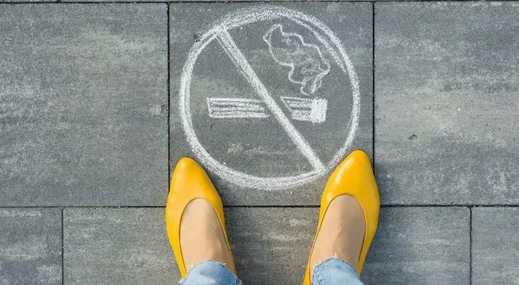 Женщина стоит над знаком 'Не курить' на тротуаре