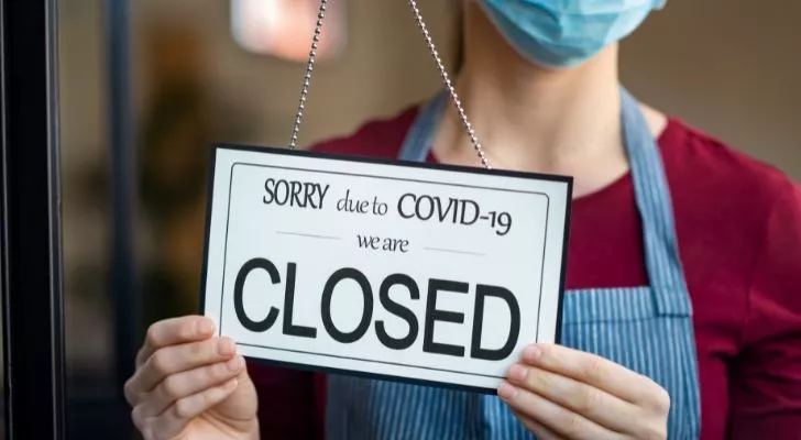 Женщина в маске ставит'closed due to COVID-19' sign in the window