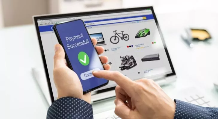 Ноутбук показывает онлайн-продукты, доступные для покупки, в то время как человек держит телефон, показывающий'Payment successful'