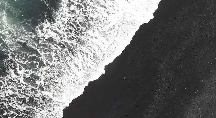 Волна разбивается о пляж с черным песком