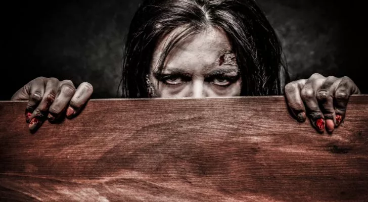 Женщина-зомби, выглядывающая из-за деревянной доски