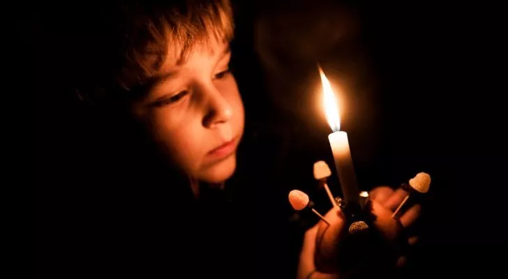 Ребенок в темноте подносит зажженную свечу к лицу